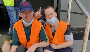 two men wearing orange high vis vests are smiling at the camera